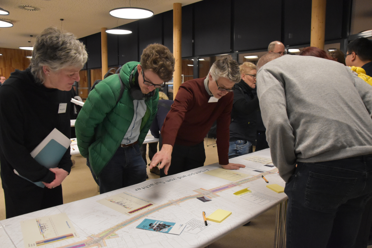 Mehrere Menschen stehen an einem Tisch mit den Plänen der Stadtbahn und diskutieren